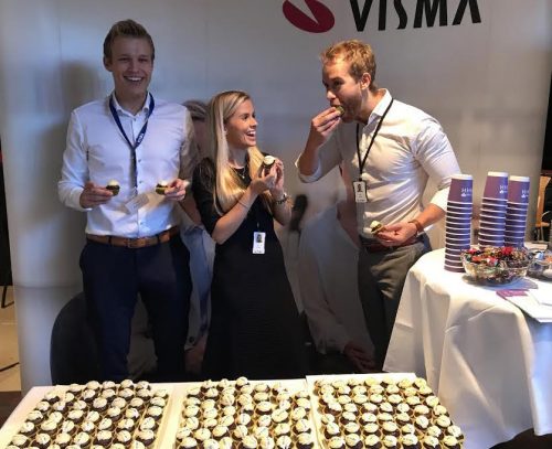 Management trainees on Visma stand holding cupcakes