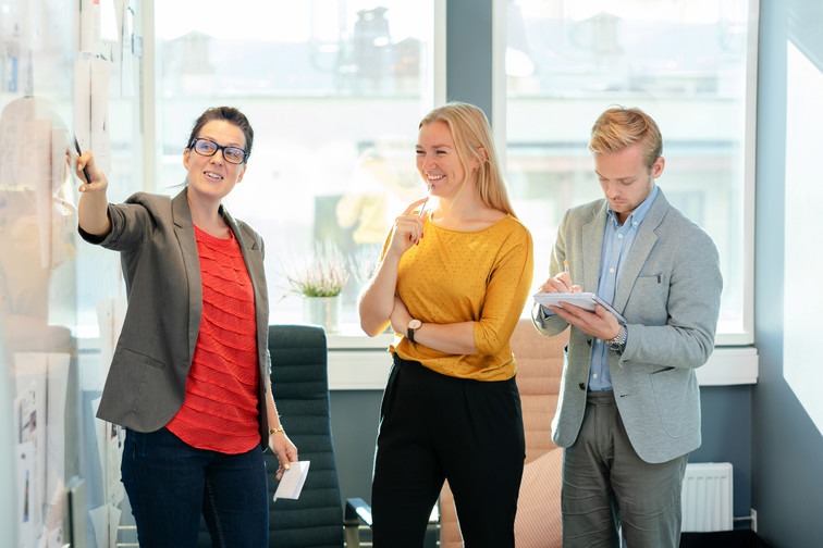 Three Visma employees brainstorming on a wall with pen and paper