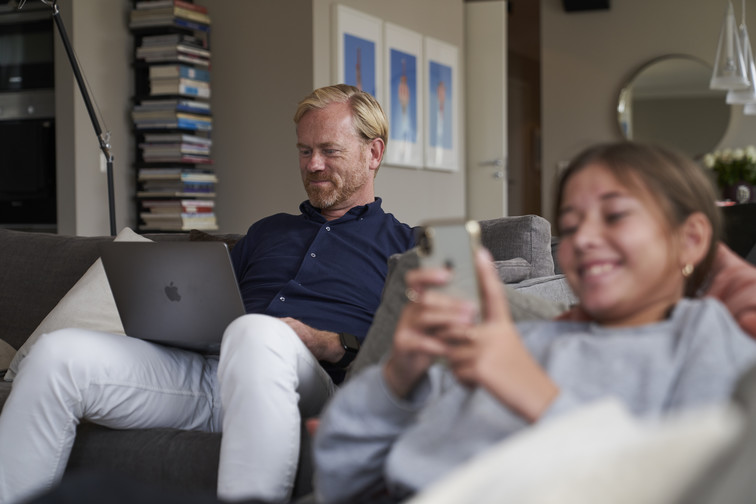 Man and girl sitting in a sofa looking at a laptop and mobile phone