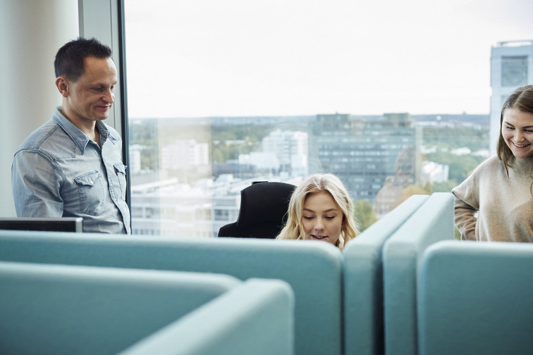 Three work colleagues have a conversation in front of a window.