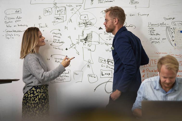 Two colleagues discuss a diagram they have drawn on the whiteboard.