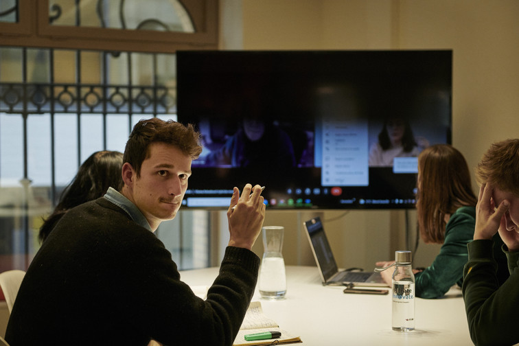 A man looks back at the camera while in a meeting with colleagues.