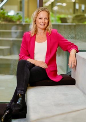 Nicoline Weih, CSR Manager at Visma e-conomic, sits on the stairs and smiles at the camera.